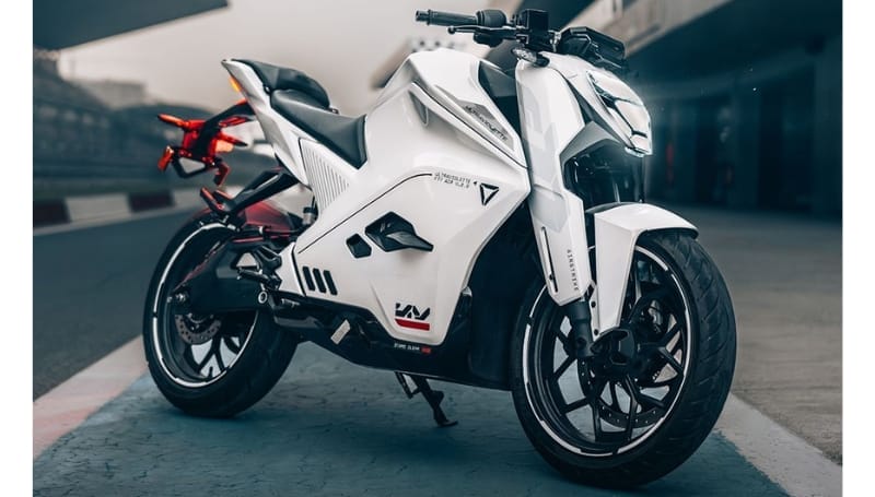 A modern white motorcycle, the F77 MACH 2 from Ultraviolette Automotive, is parked on a paved surface. Featuring a sleek design with sharp angles and red accents on its rear components, this bike offers an in-depth look at cutting-edge engineering and style.