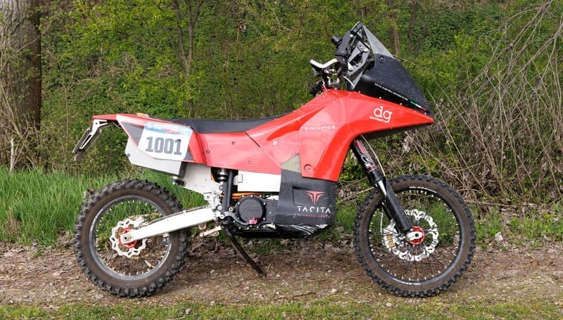 Red and white off-road motorcycle parked on a grassy area with trees in the background.
