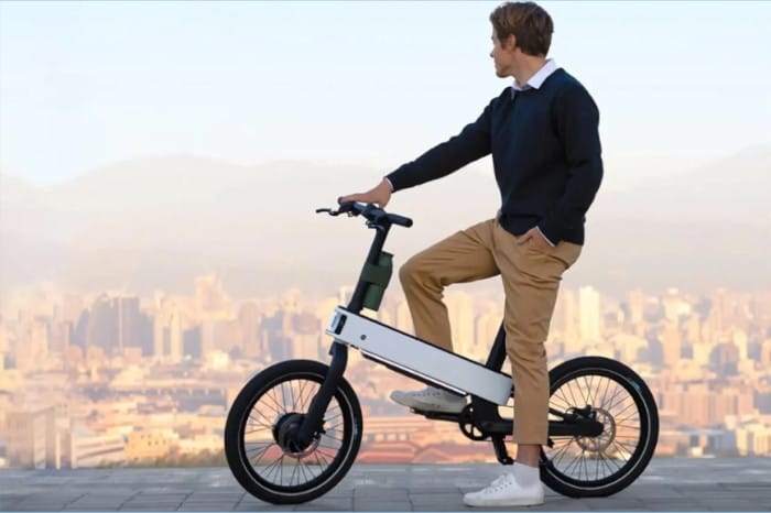 A man standing next to the best foldable electric bike for your lifestyle, overlooking a cityscape from a high vantage point during daylight.