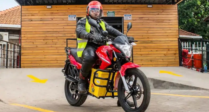 A person in a black jacket and red helmet rides a red <a href=