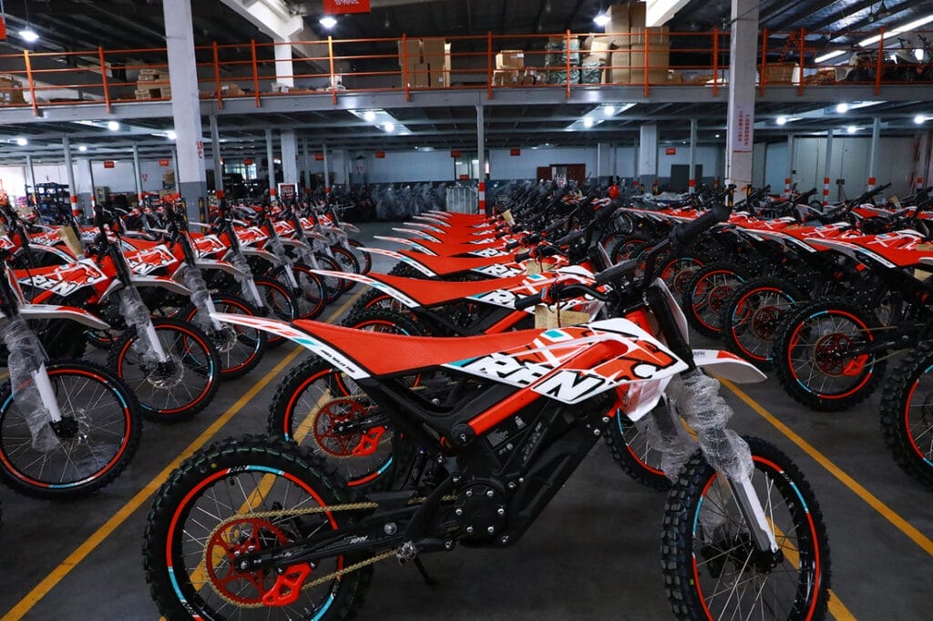 Multiple dirt bikes, including Apollo's RFN Electric Motorbike Upgrades, parked in a warehouse.
