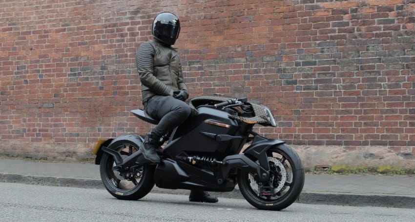As electric motorbikes gain popularity, a man sits astride an Arc Vector one in front of a brick wall, radiating an aura of speed.