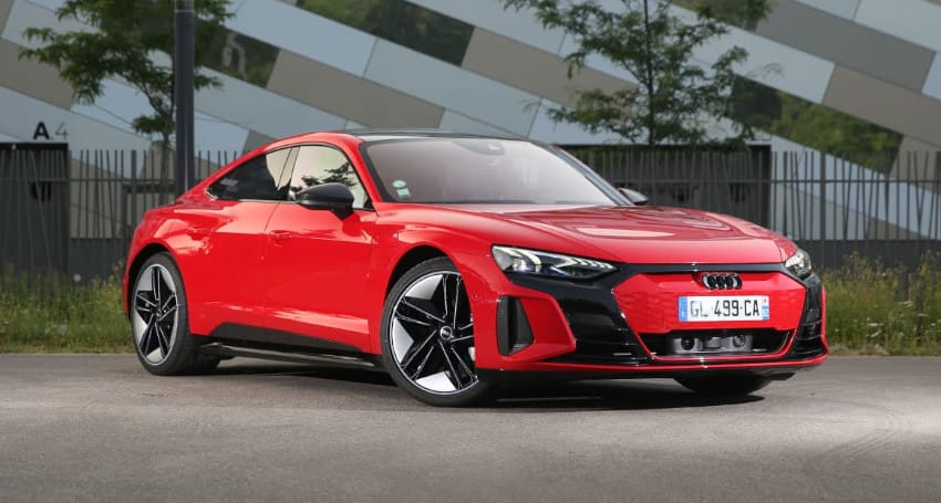 Red electric Audi sports car parked outside a modern building, featuring sleek design, alloy wheels, and prominent headlights.