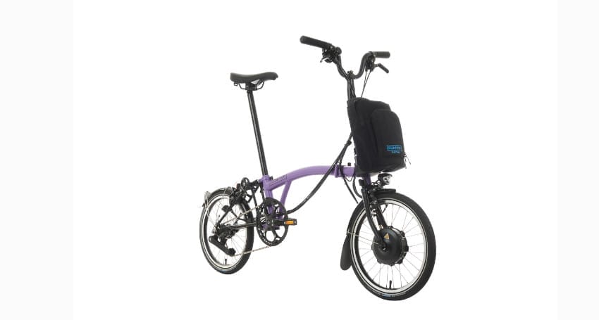 A purple folding Brompton Electric C line Urban bicycle with front and rear wheels, a black seat, and a black bag mounted on the front—designed to be the lightest electric bike available.