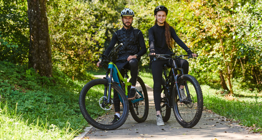 Two cyclists wearing helmets and black outfits pose with their <a href=