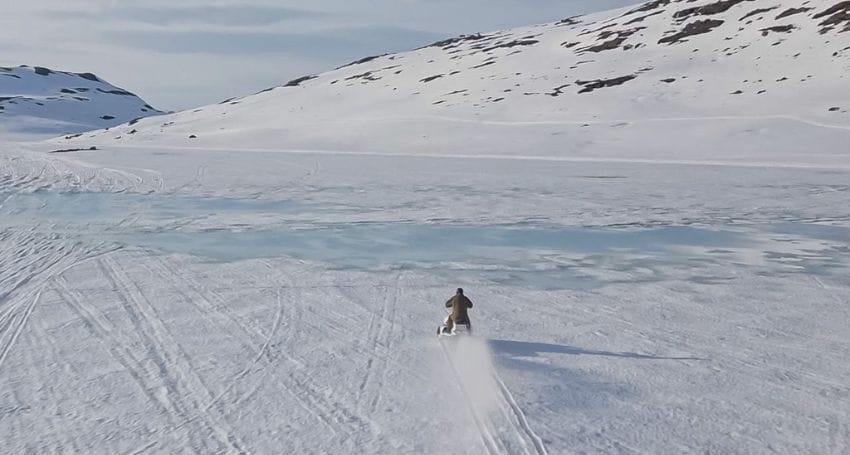An aerial view of a person on an electric snowmobile in the snow.