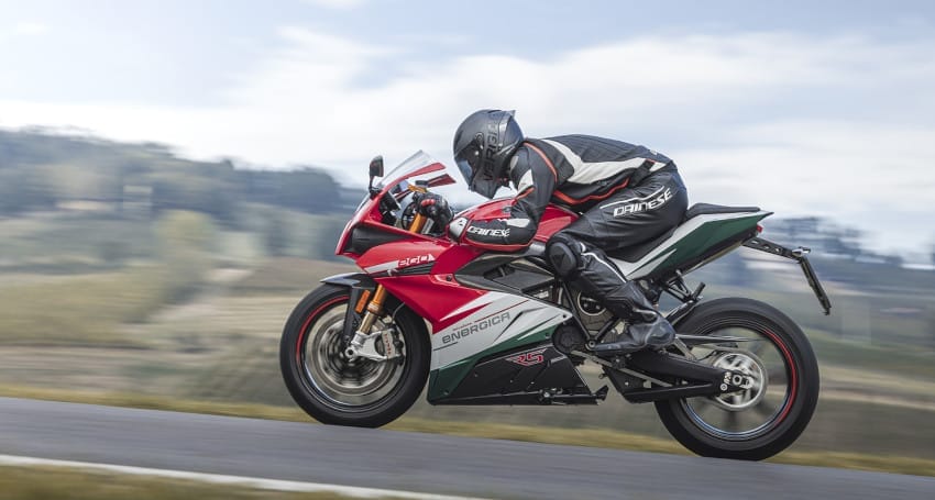 A motorcyclist in racing gear rides a red, white, and green sport motorcycle on a paved track with a blurred background.