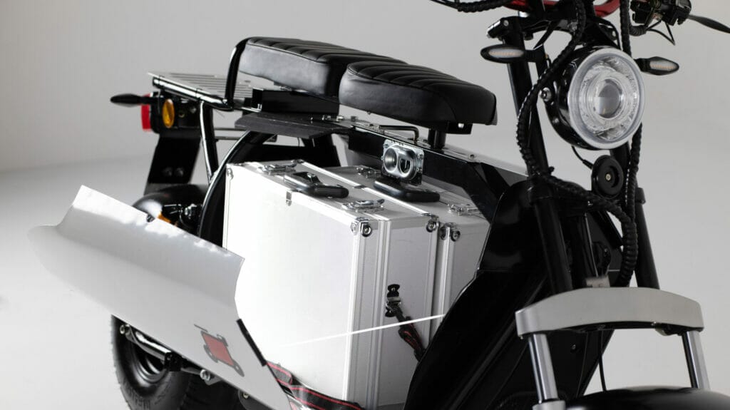 A black and white electric scooter with a suitcase on it.