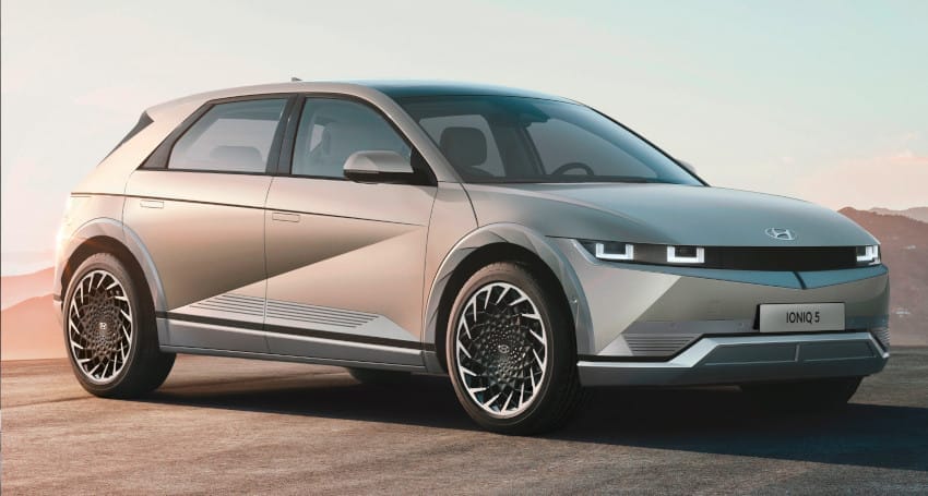 A silver hyundai ioniq 5 electric car parked outdoors with a mountainous backdrop during sunset.