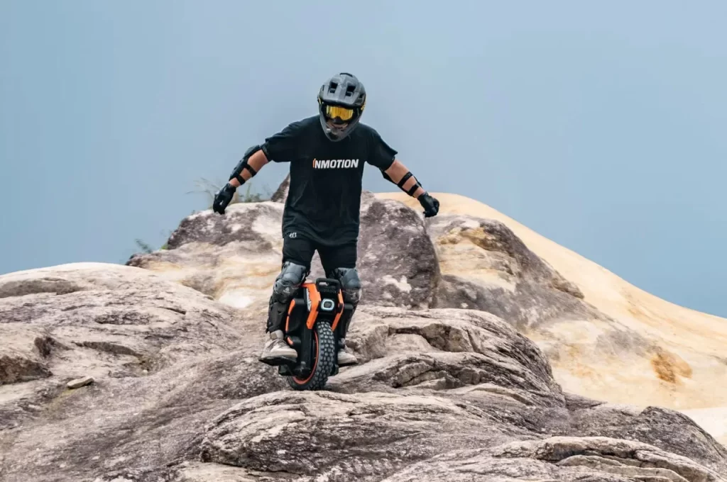 A person riding a powerful orange mountain bike on rocky terrain.