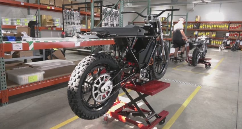 A mechanic is working on an electric motorbike placed on a hydraulic lift in a garage equipped with shelves full of tools and parts in the background, reflecting the growing trend of electric motorbikes in Europe.