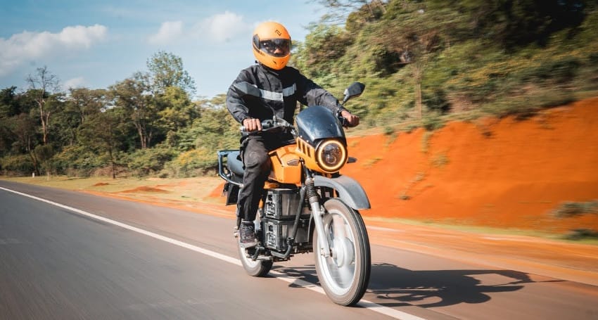 A man riding an orange motorcycle down a road in Kenya.