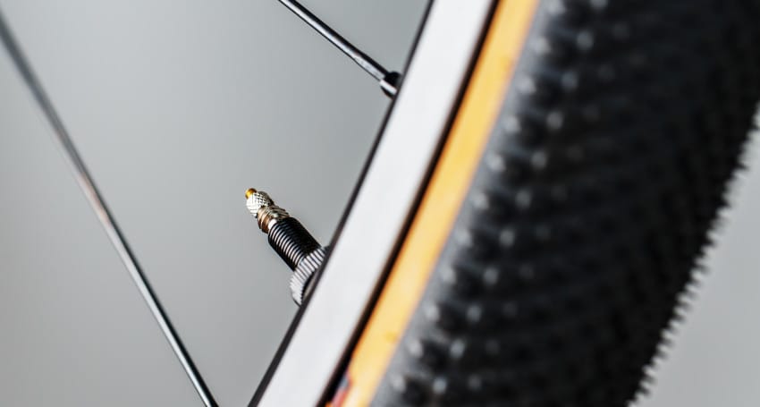 Close-up of an e-bike tire valve attached to a thin, metal rim, with a detailed view of the tire tread against a blurred gray background.