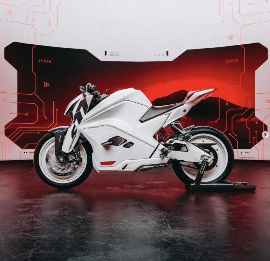 The Ultraviolette F77, a white motorcycle, is parked in front of a red background, holding the Long-Distance <a href=