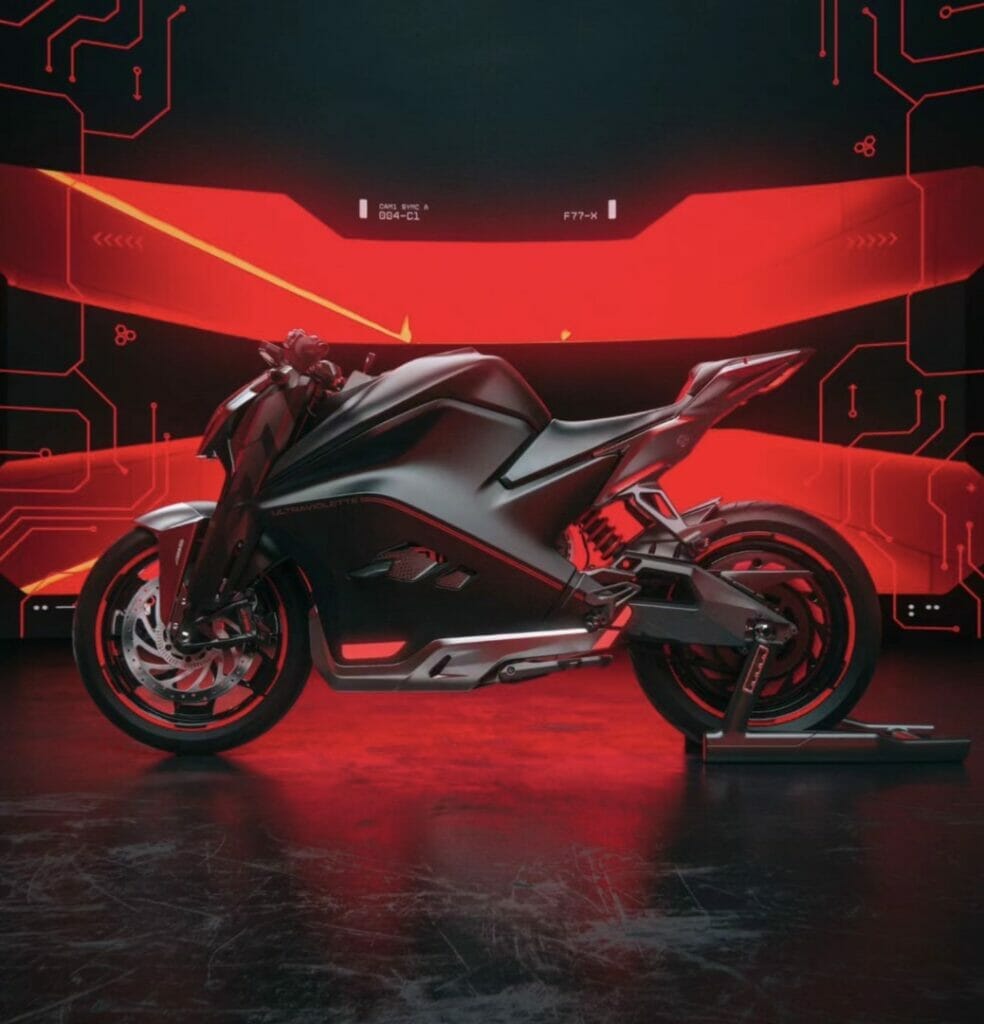 A futuristic Ultraviolette F77 motorcycle is parked in front of a red light.