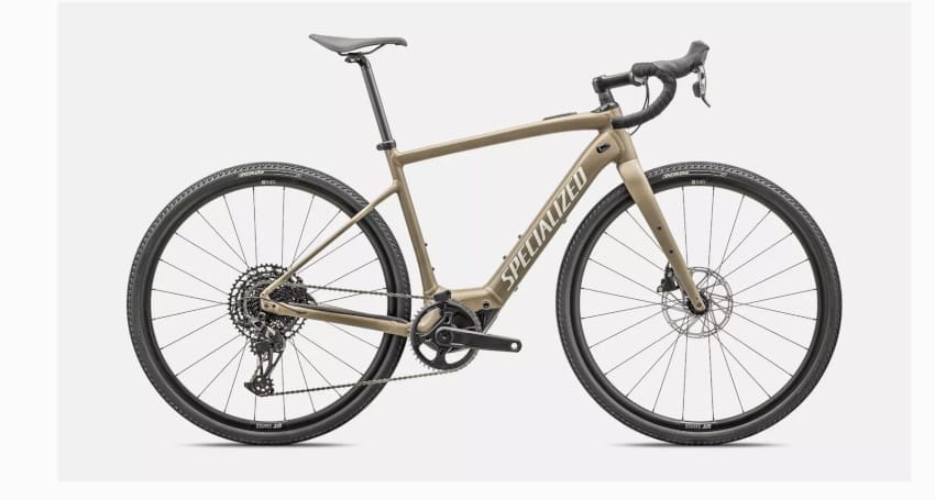 A tan-colored Specialized Turbo Creo road bike with drop handlebars, disc brakes, and a chain-driven gear system. Touted as one of the lightest electric bikes available, the bike is shown in profile against a plain white background.