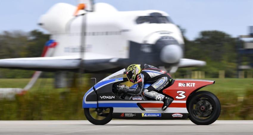 A Voxan Wattman electric motorbike speeding in front of a space shuttle.