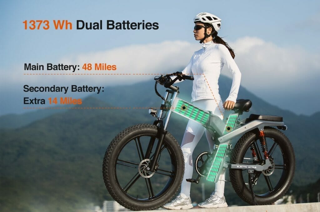 A woman is standing on a bike with dual batteries.