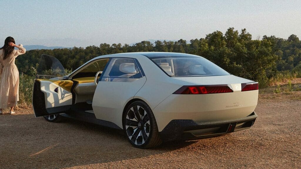 A woman is standing next to a minimalist BMW Vision Neue Klasse Concept car on a dirt road.