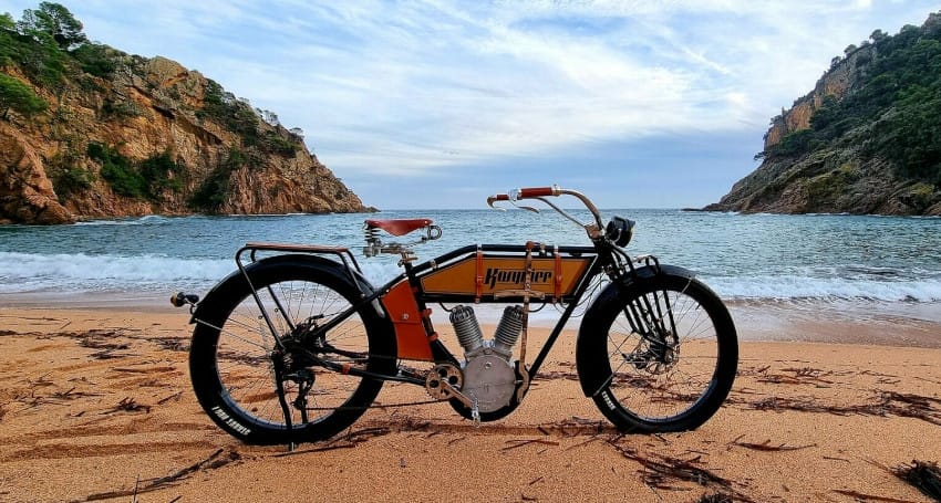 An old ebike sitting on the sand next to the ocean.