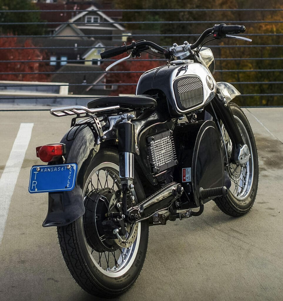A seamless electric conversion has transformed a 1967 Honda CA160 Dream Motorcycle into a silent black and white beauty parked in a parking lot.