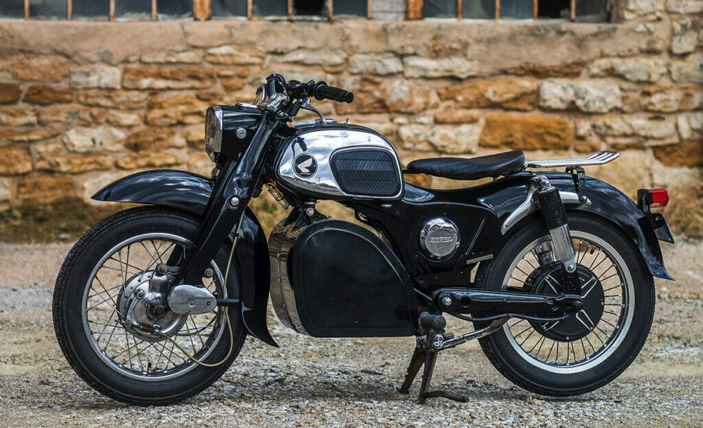 Silent beauty: A 1967 Honda CA160 Dream motorcycle transformed into a black and silver seamless electric conversion, parked in front of a stone wall.