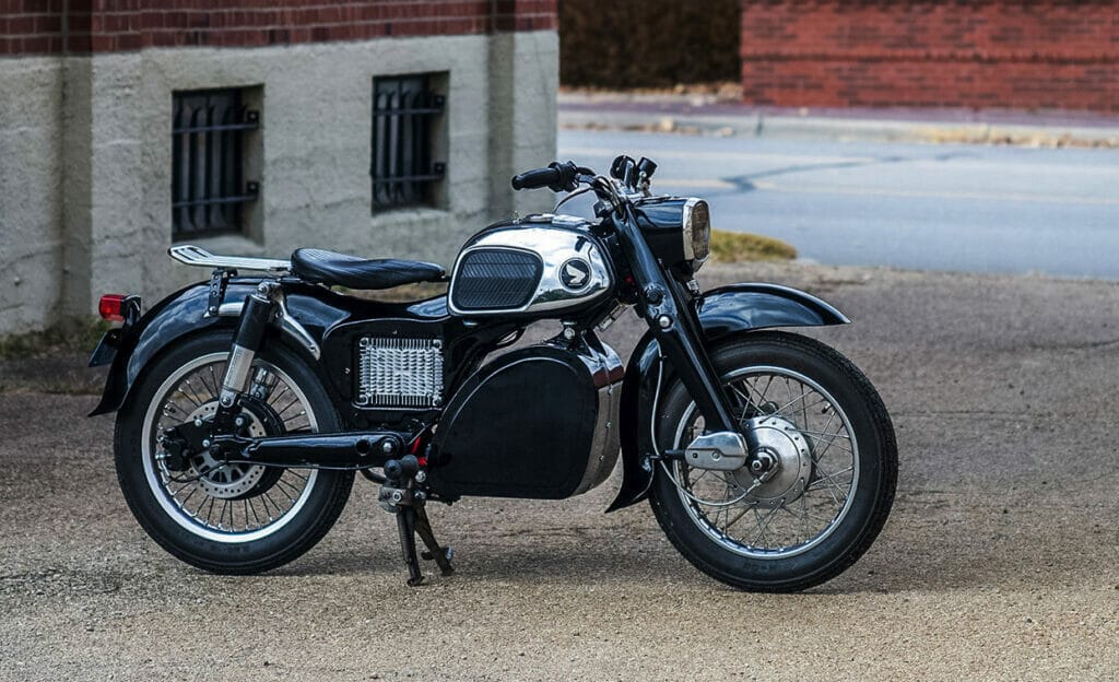 A black and white motorcycle transformed into a silent beauty through seamless electric conversion, parked in front of a brick building.