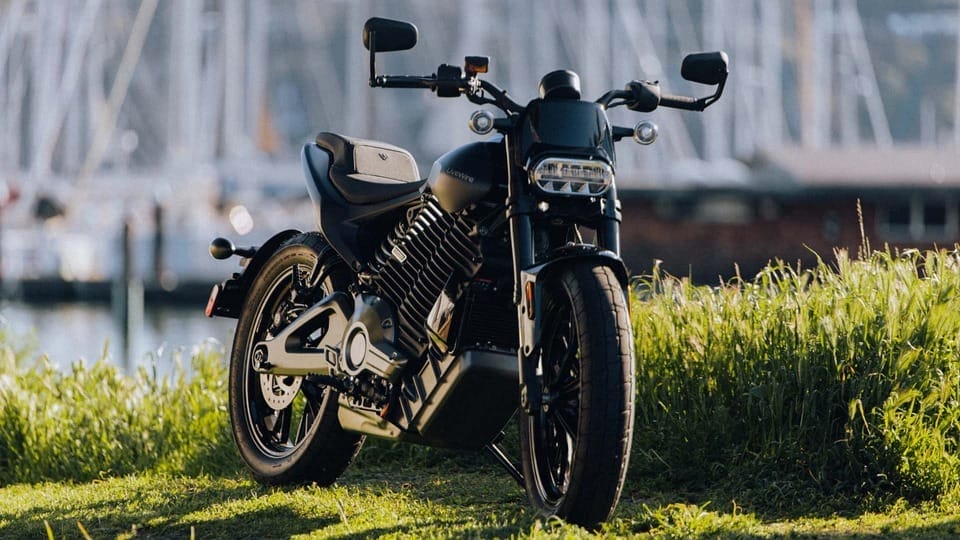 A black motorcycle parked on the grass near a boat.