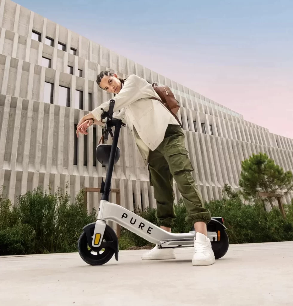 A man leaning on an electric scooter in front of a building.