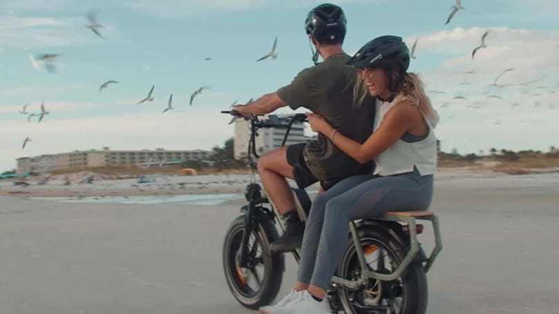 A man and woman enjoying a ride on their Dual Batteries electric bike along the sandy beach.