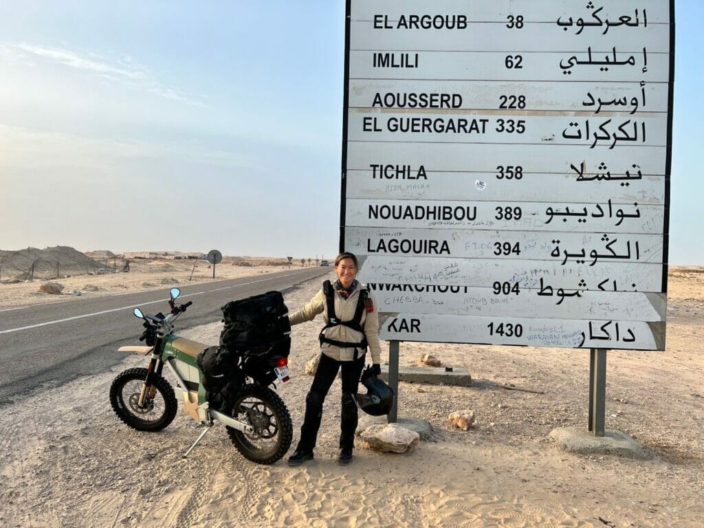 A woman standing next to a sign in the desert.