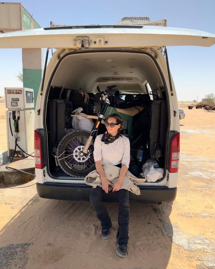 A man sitting in the back of a van with his motorcycle.