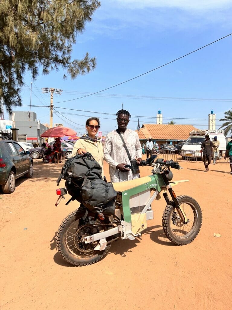 Two people standing next to a motorcycle on a dirt road.