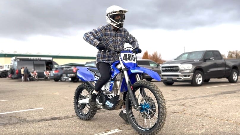 A man riding a blue dirt bike in a parking lot.