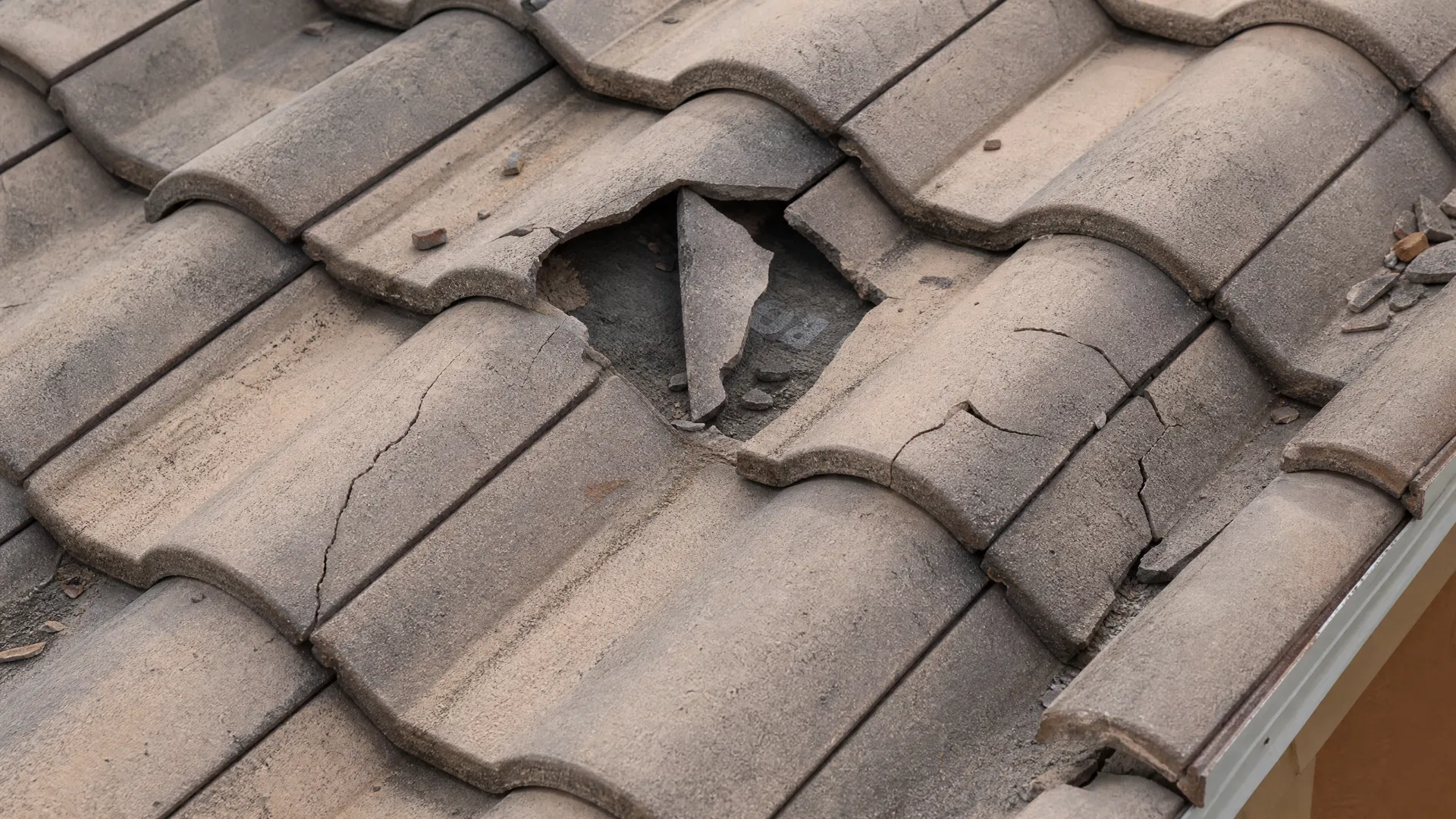 Close-up of cracked and shattered concrete roof tiles on a Florida home with underlayment visible beneath a broken tile