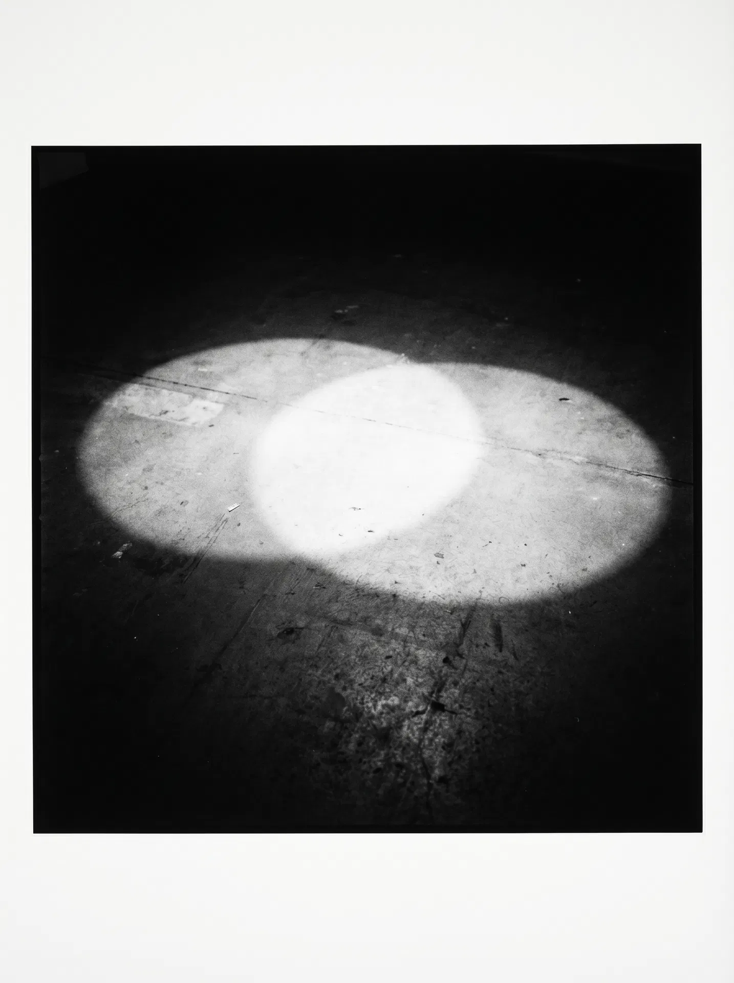 Two circles of light on a dark floor — cast from two separate sources — overlapping at their edges to create a third, brighter zone. The overlap zone is the most luminous area of the frame. Fuji X-Pro1 aesthetic, Ming Smith and Deana Lawson observational lineage.