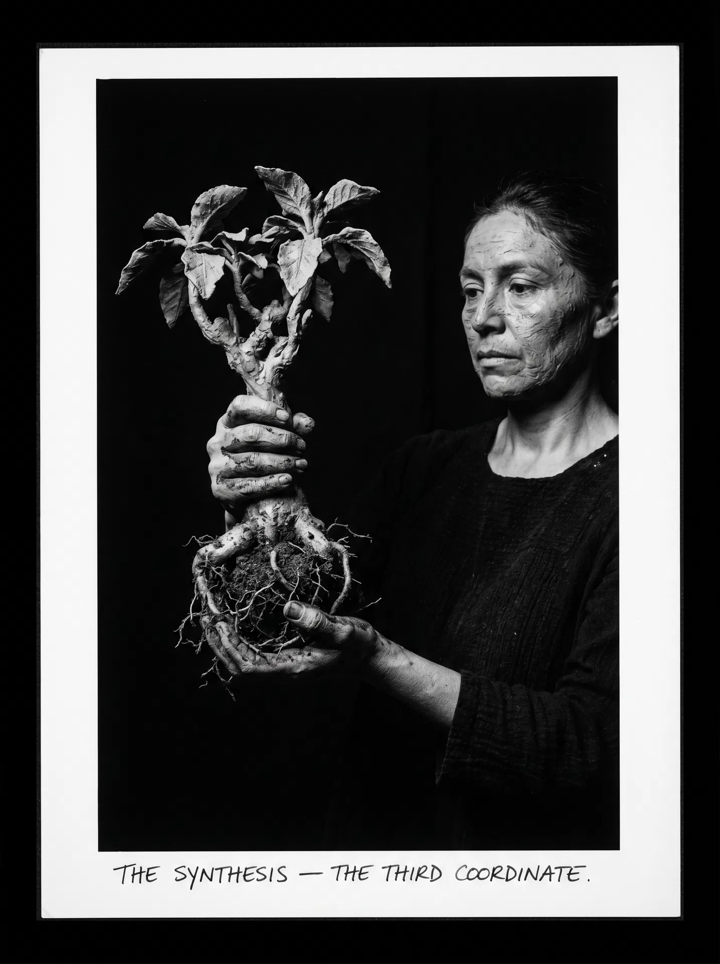 A woman holds a plant — roots exposed, earth still clinging — in front of her body. The roots and her hands are the same texture. The plant and the woman are the same material. The background is absolute black. Fuji X-Pro1 aesthetic, Lola Álvarez Bravo and Samantha Box observational lineage.