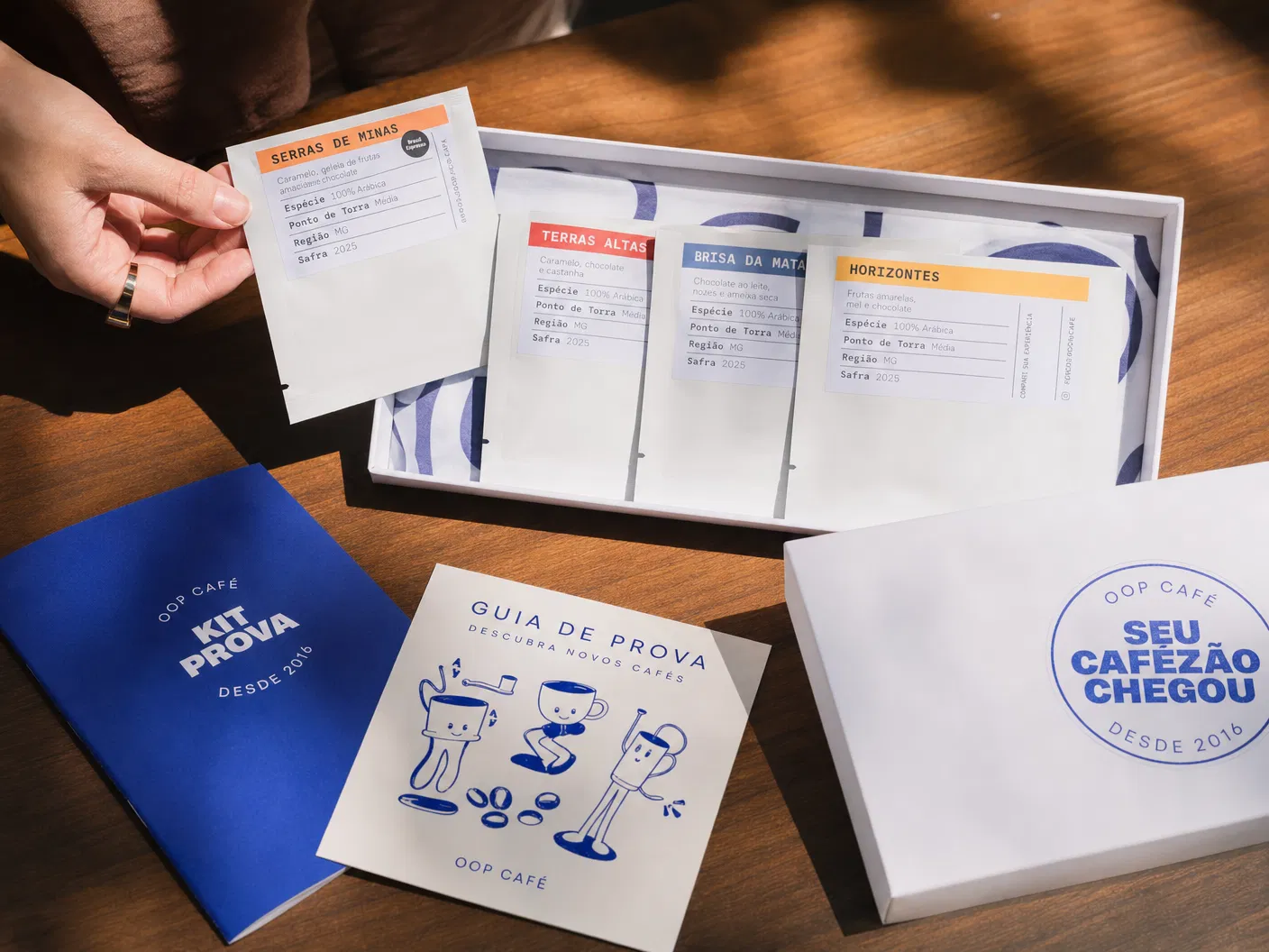 Kit Prova OOP aberto sobre a mesa, com sach�s, cart�o azul e materiais de degusta��o.