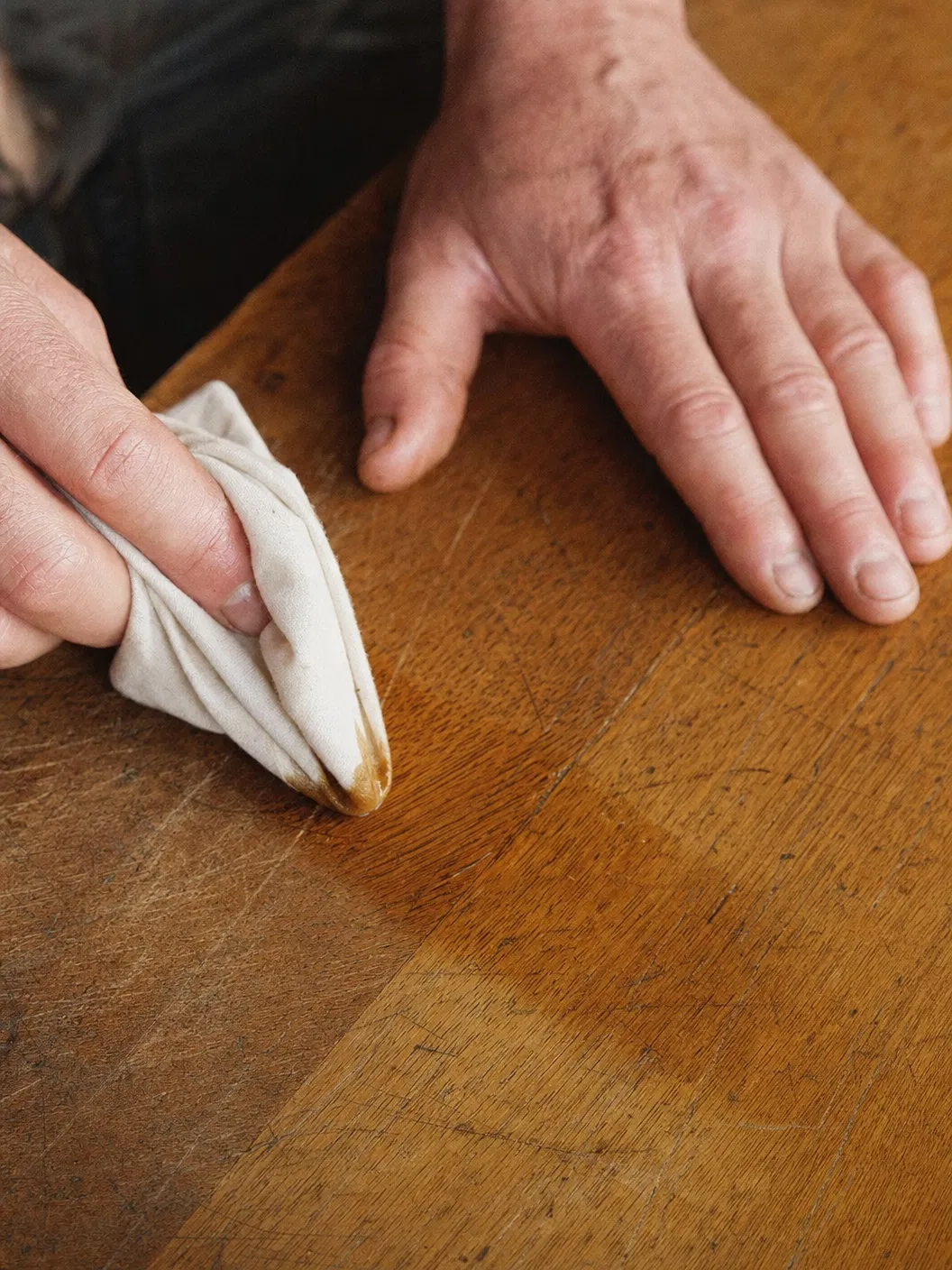 Hands applying Luxgrove salve to scratched oak table
