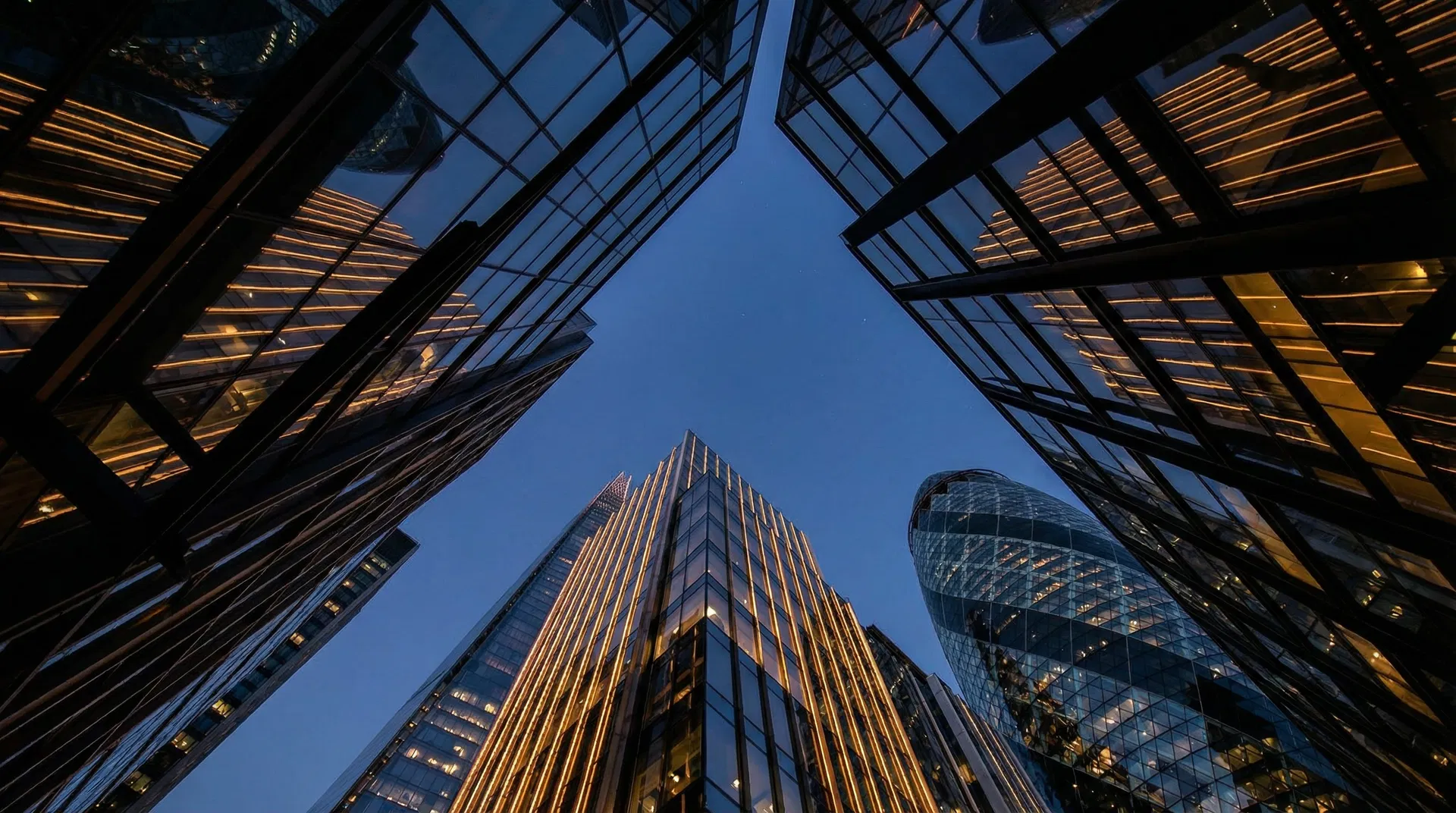 Modern glass skyscrapers viewed from below against a dark sky