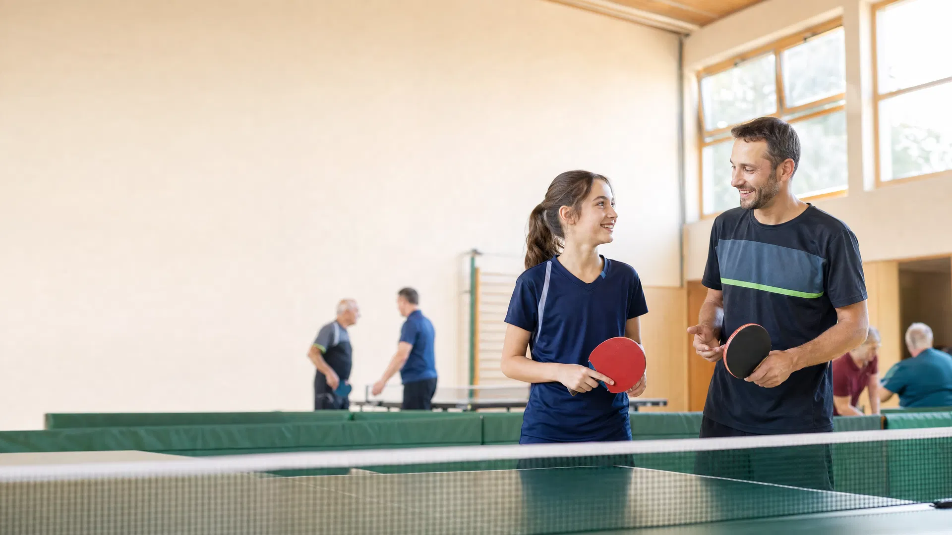 Einsteiger und Trainer in einer hellen Tischtennishalle als freundliches Hero-Bild der Zugangsseite