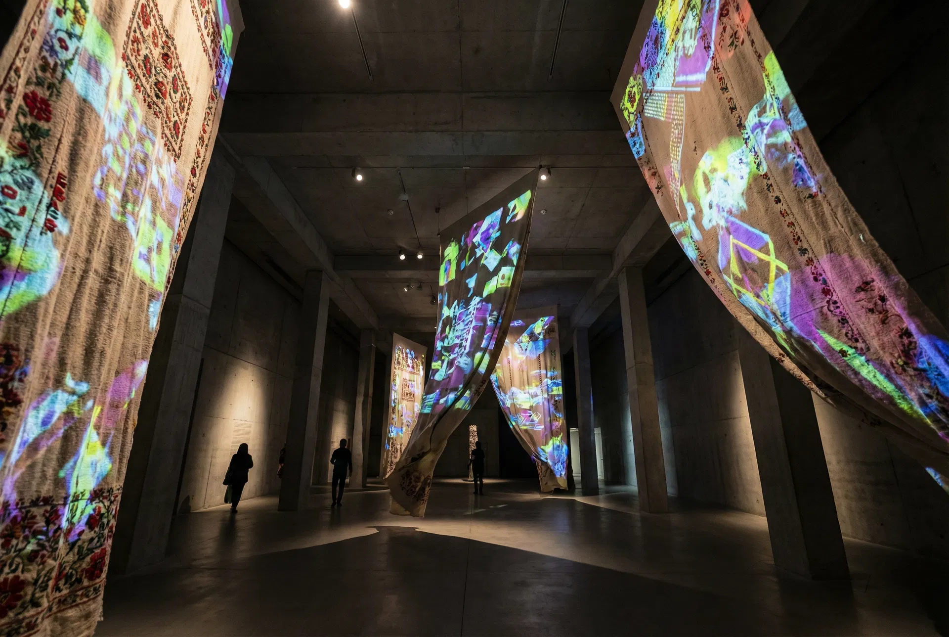 Instalação artística no MASP com tecidos bordados e projeções de luzes e padrões gerados por IA