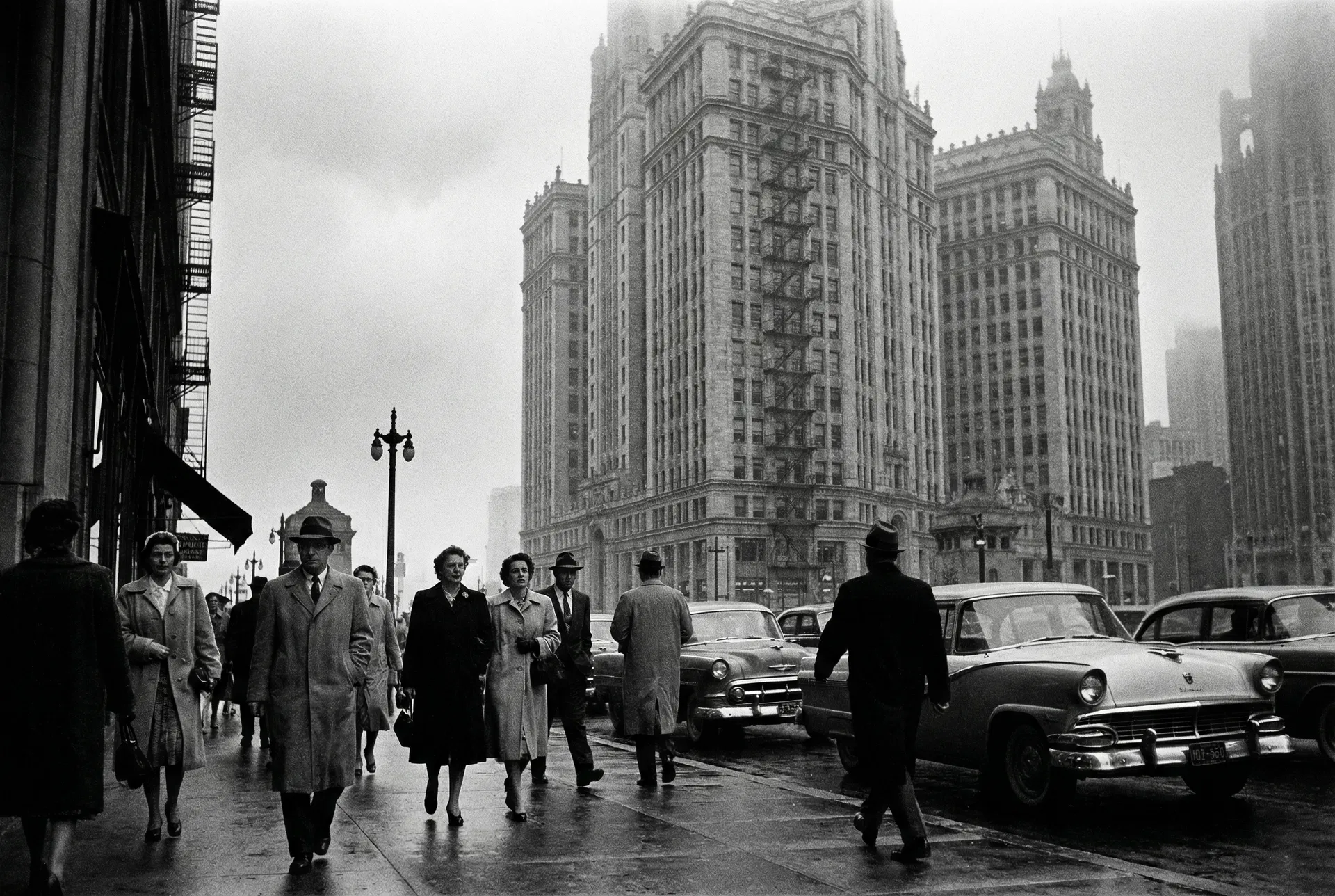 Cena de rua em Chicago nos anos 1950, com pessoas caminhando e edifícios ao fundo, em preto e branco