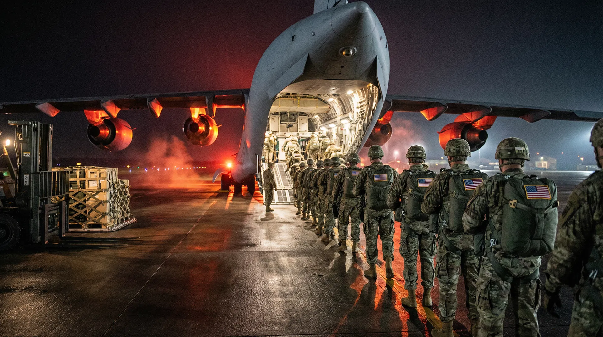 US soldiers from the 82nd Airborne Division boarding a C-17 transport aircraft at night.