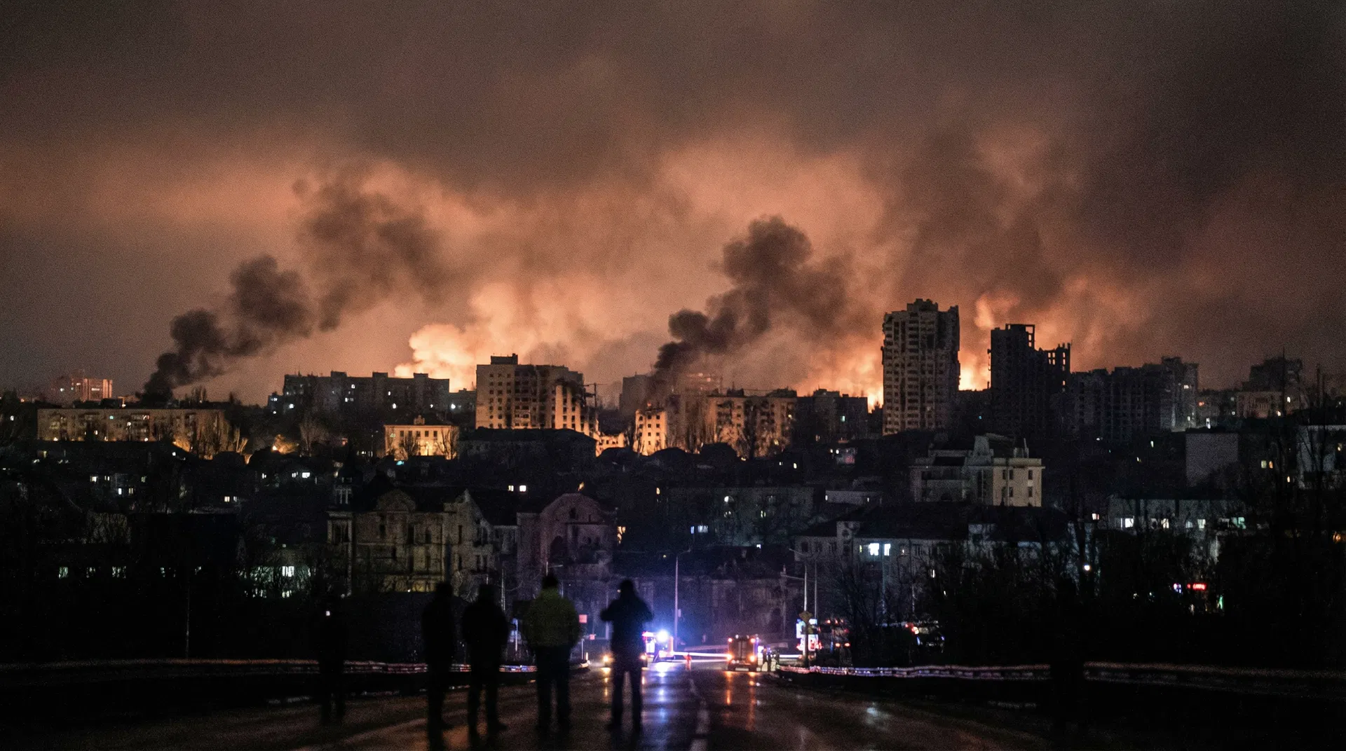 Nighttime cityscape of Beirut with smoke rising from multiple neighborhoods and fires illuminating the dark sky