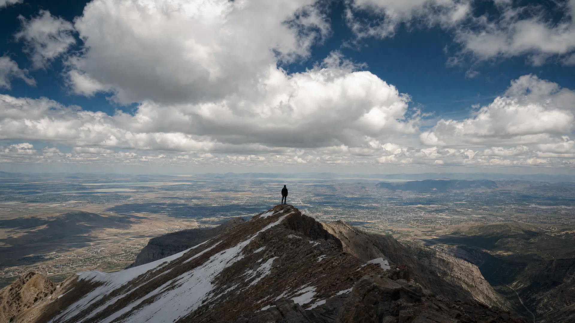 Lone hiker standing on a rocky ridgeline on Mount Timpanogos looking over the vast Utah Valley below