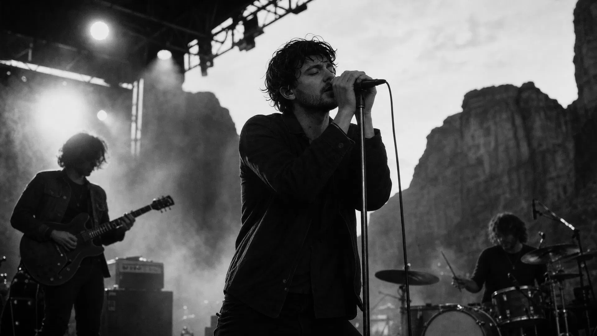 Moody black and white concert photograph of an indie rock band performing on an outdoor stage with canyon walls behind