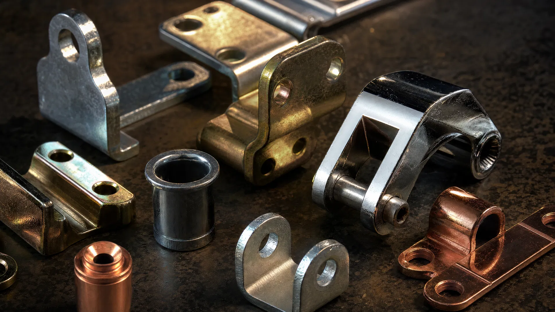 Verschiedene galvanisch beschichtete Metallteile – vernickelt, verchromt und verkupfert – auf dunkler Industrieoberfläche