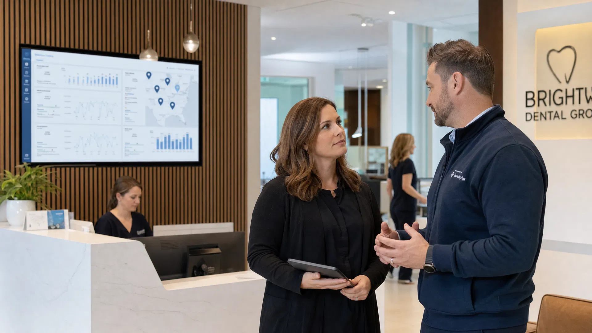 Operations leaders inside a modern multi-location dental group reception area discussing visibility performance