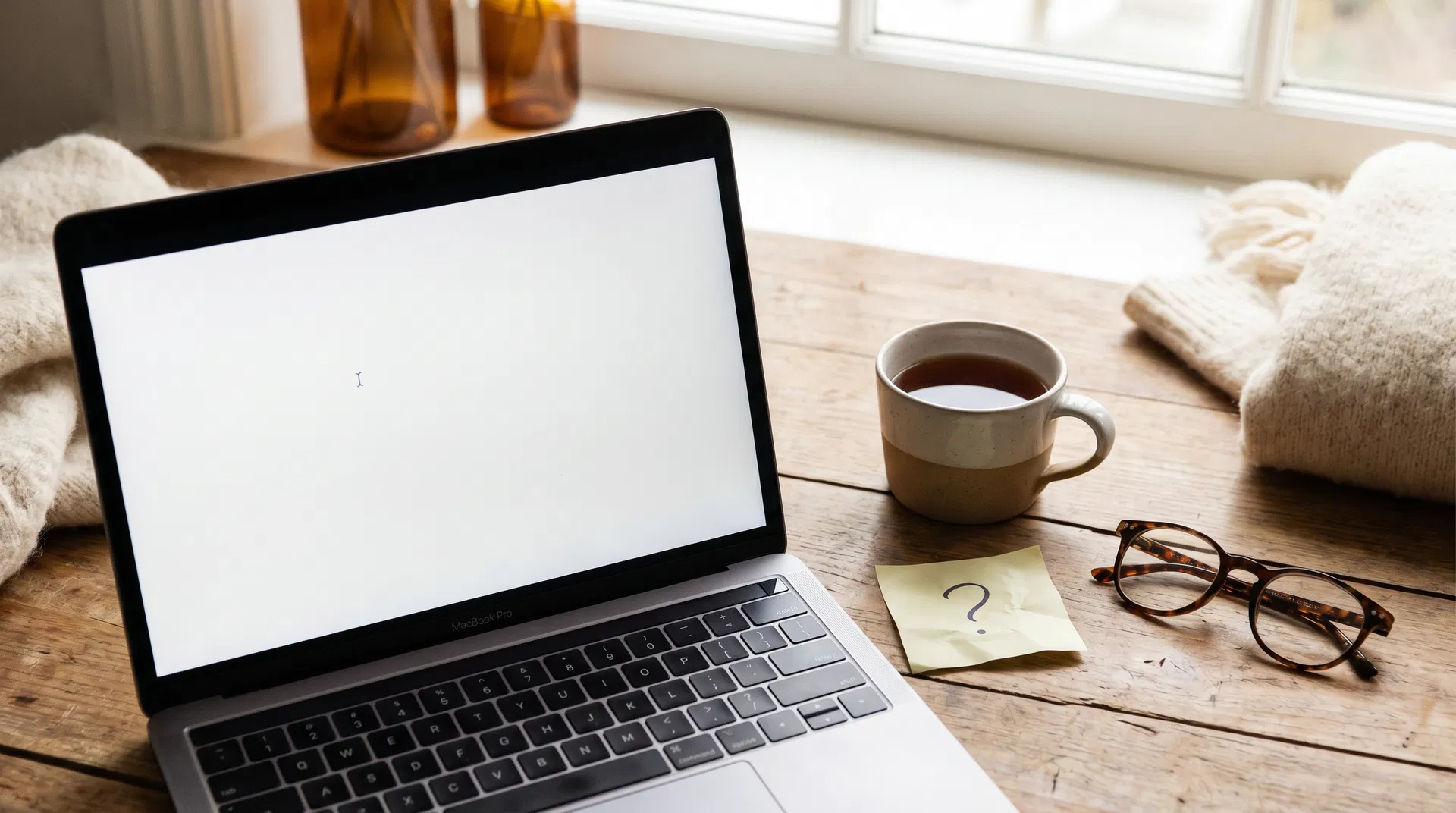 Laptop with blinking cursor on a blank screen, tea and reading glasses nearby — the moment before beginning with AI